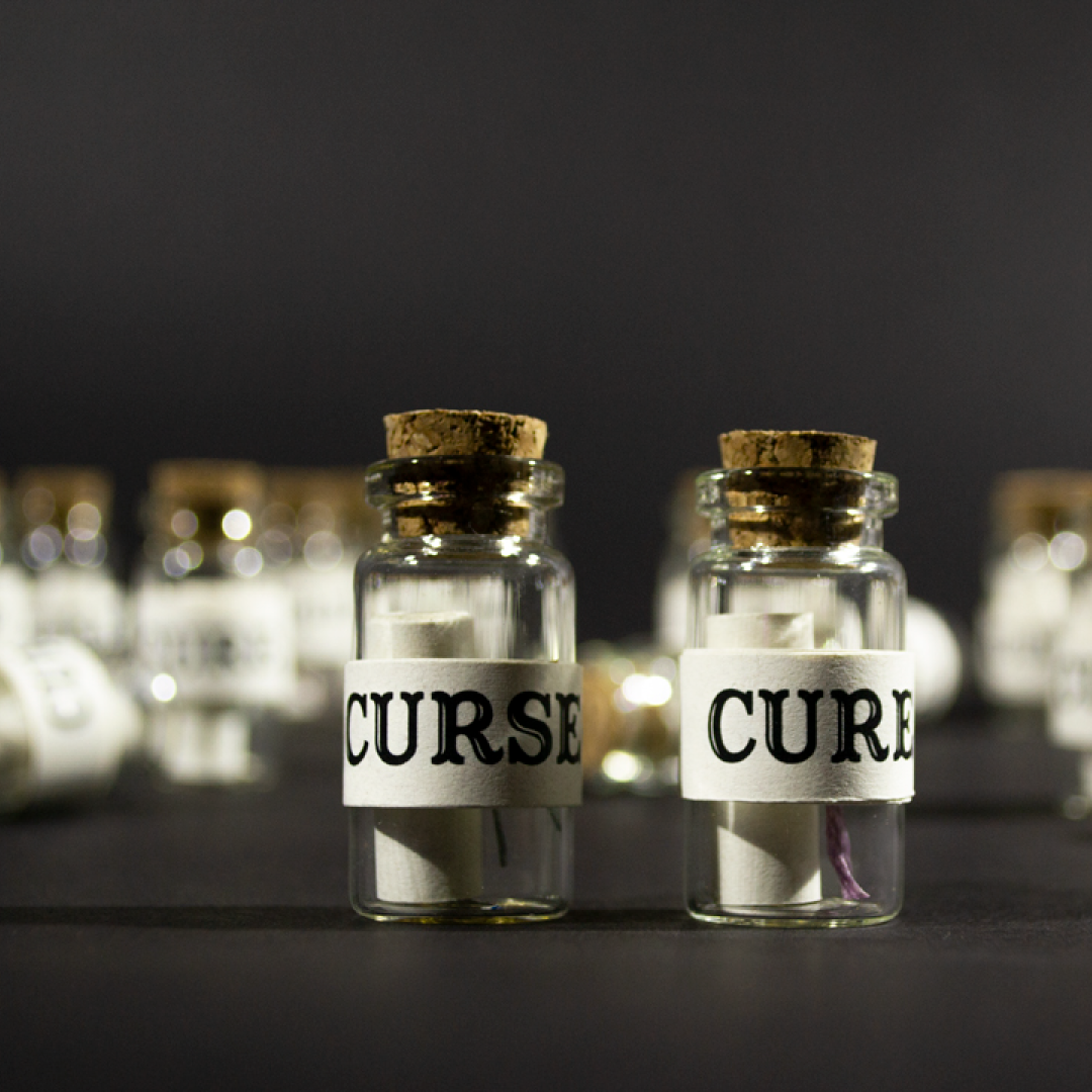 Cures & Curses product shot. A photo of two small glass bottles with a scroll inside. The outsides are wrapped in paper and labelled cure & curse.