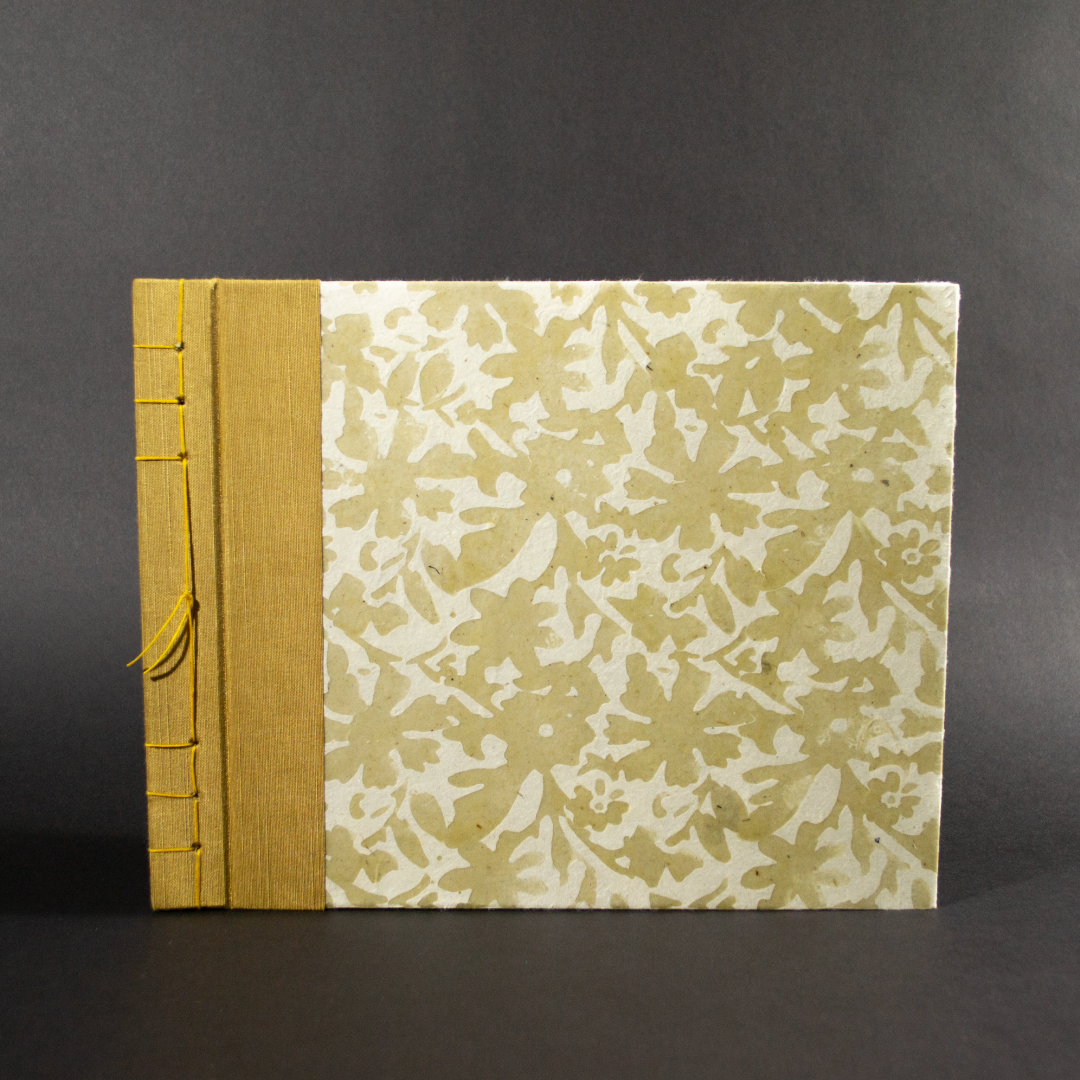 Stab bound floral photo album has gold book cloth on the left side and the paper has a waxed floral pattern
