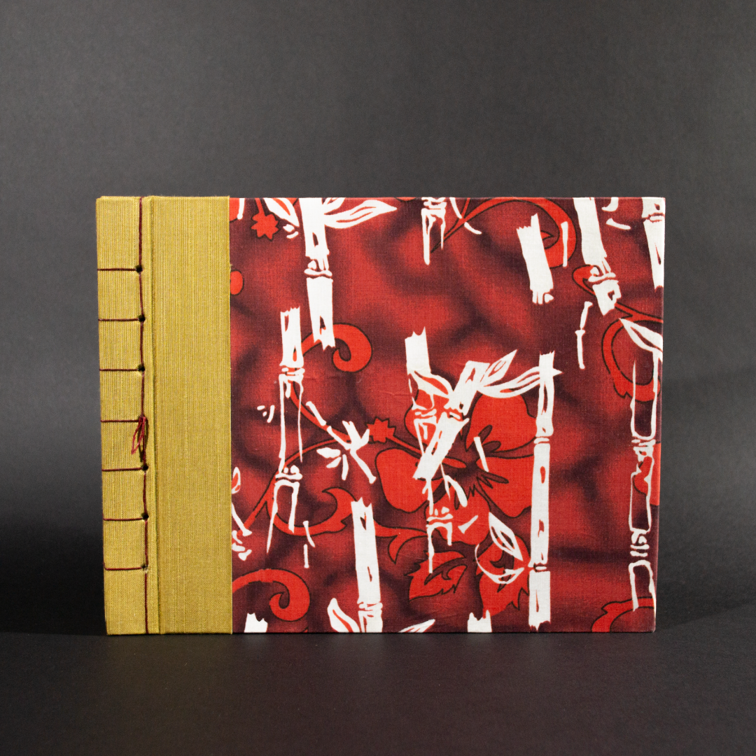 Stab bound Hawaiian photo album has gold book cloth on the left side and a Hawaiian floral pattern with bamboo and hibiscus