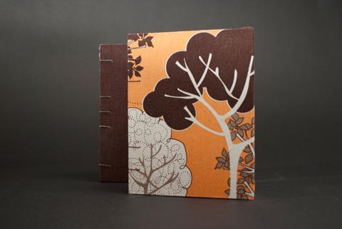 This photograph is two optic stitch books, one brown, and one with orange and brown trees. It's a promotional studio photo for the coptic duo class by Laurel Tree Bindery.
