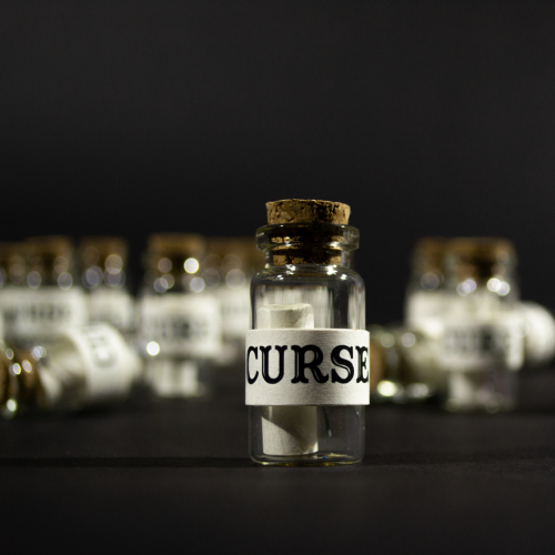 Curses product shot. A photo of a small glass bottle with a scroll inside. The outside is wrapped in paper and labelled curse.