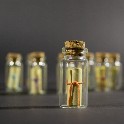 Message in a Bottle product shot with one bottle in focus in the foreground. Inside the bottle is a rolled up scroll.