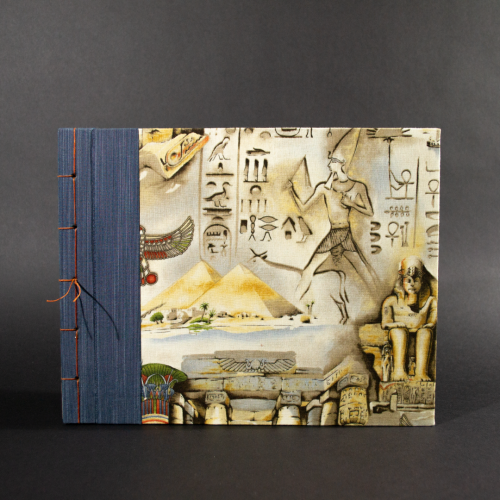 Front cover of stab bound Egyptian photo album showing the blue book cloth left side and a with Egyptian themed fabric featuring a pharaoh, pyramids, and hieroglyphics.