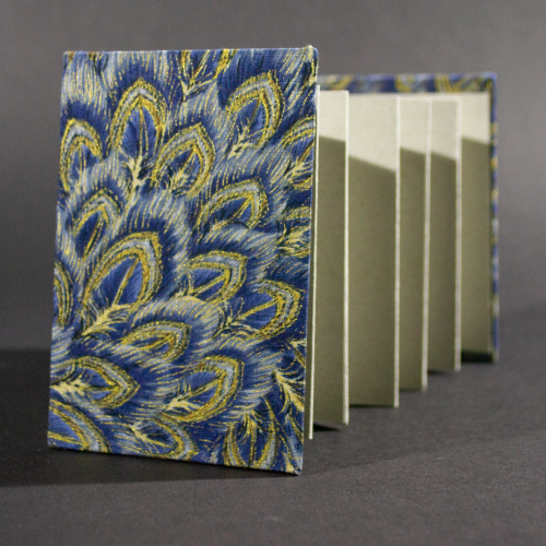 The front cover of the peacock medium accordion book has peacock feathers in blue and gold with heavy gray inside pages.