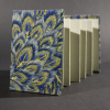 The front cover of the peacock medium accordion book has peacock feathers in blue and gold with heavy gray inside pages.
